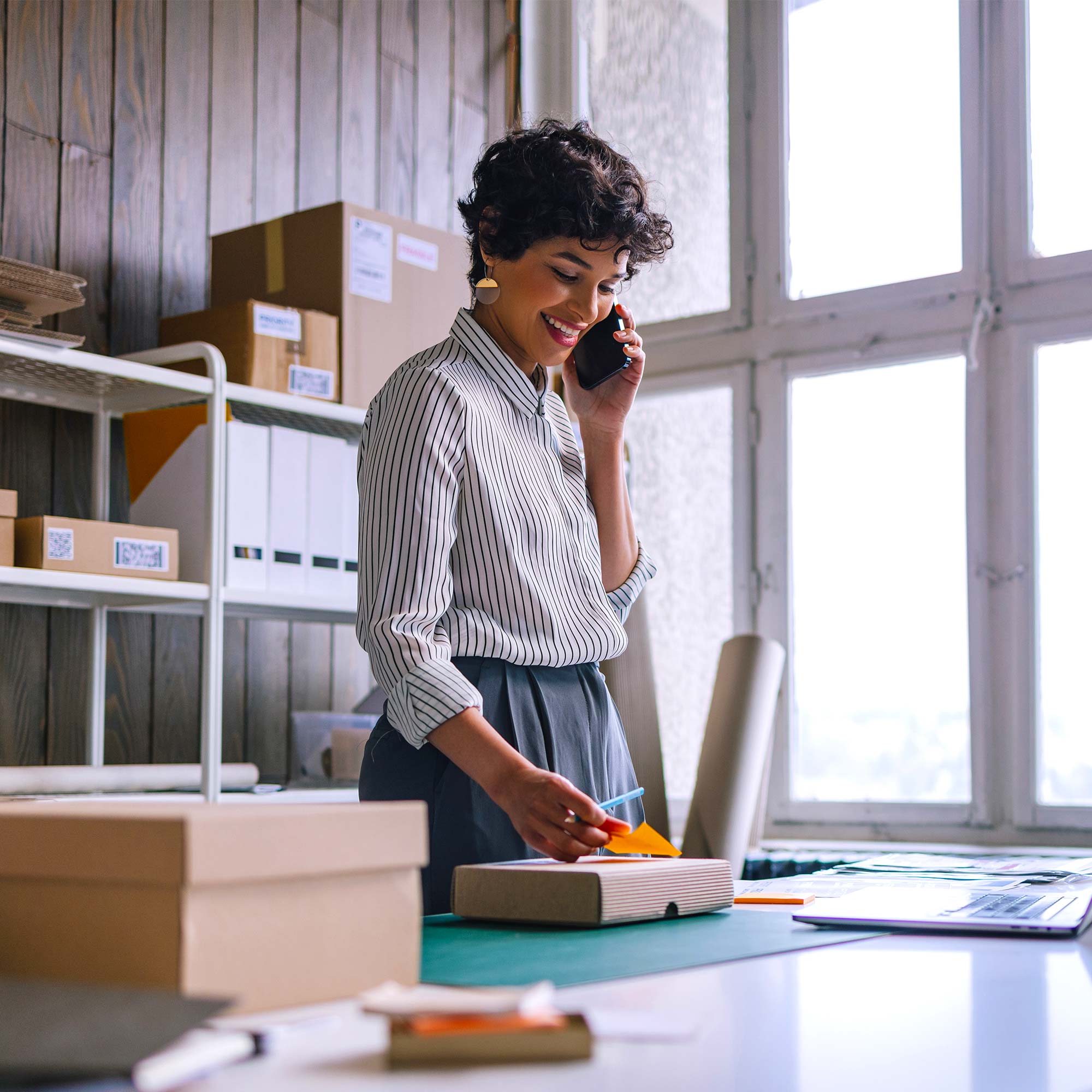 A woman stands in her place of business and talks on the phone.
